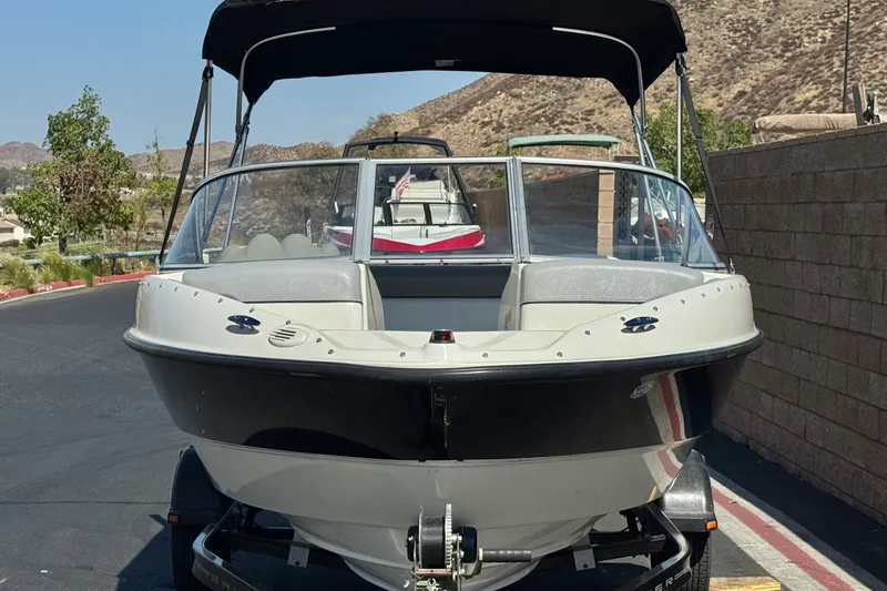 Slide: The Image of 2011 Bayliner 185 Bowrider boat on trailer, parked outdoors with scenic background. - 2