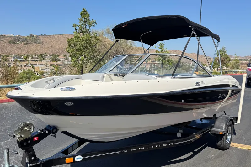 Slide: The Image of 2011 Bayliner 185 Bowrider boat on trailer, parked outdoors with scenic background. - 3