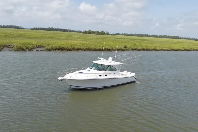Slide: The Image of 2015 Pursuit OS 385 Offshore boat cruising on a calm river near grassy shoreline. - 0