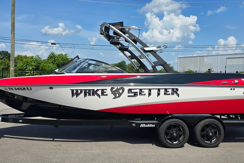 Slide: The Image of 2011 Malibu Wakesetter 247 LSV boat on trailer, red and white design, sunny day. - 2