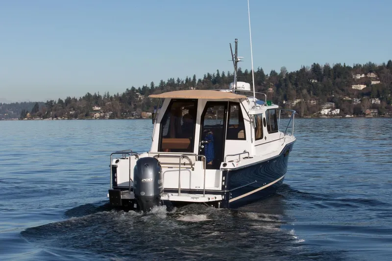 Slide: The Image of 2027 Ranger Tugs R-23 boat cruising on a serene lake with forested shoreline. - 7