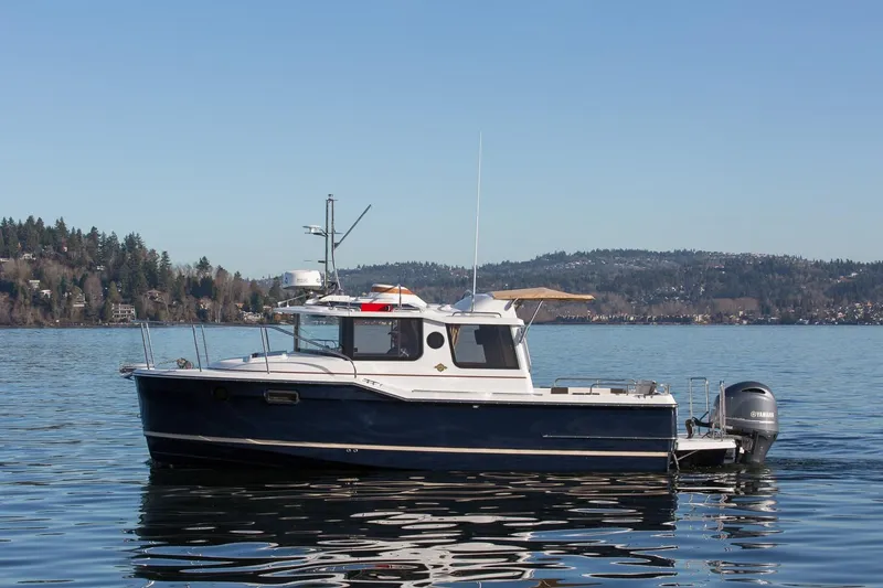 Slide: The Image of 2027 Ranger Tugs R-23 boat on a serene lake with forested hills in the background. - 1