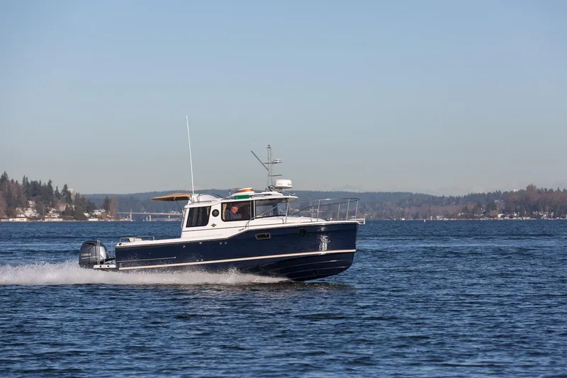 The Image of 2027 Ranger Tugs R-23 cruising on a serene lake under a clear blue sky. - 0