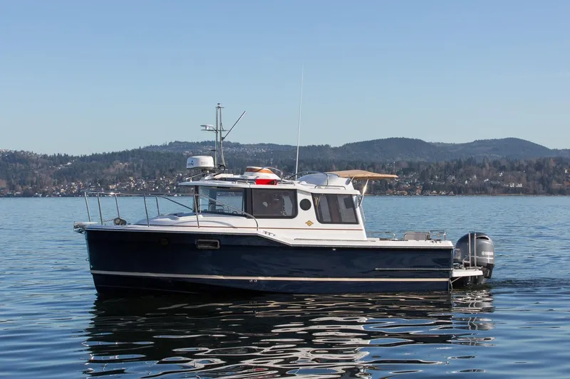 Slide: The Image of 2027 Ranger Tugs R-23 boat on a serene lake with mountainous backdrop. - 2