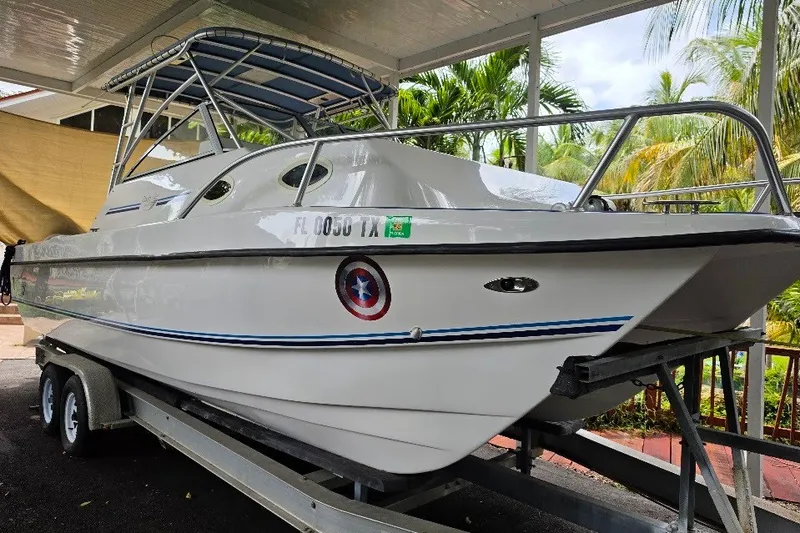 The Image of 2006 Twin Vee 26 Express boat on trailer under shelter, surrounded by tropical foliage. - 0