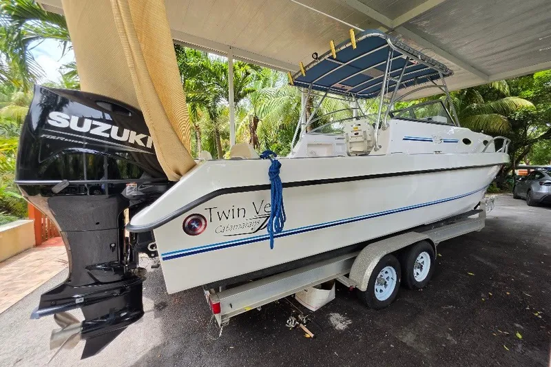 Slide: The Image of 2006 Twin Vee 26 Express boat on trailer with Suzuki outboard motor, parked under shelter. - 2