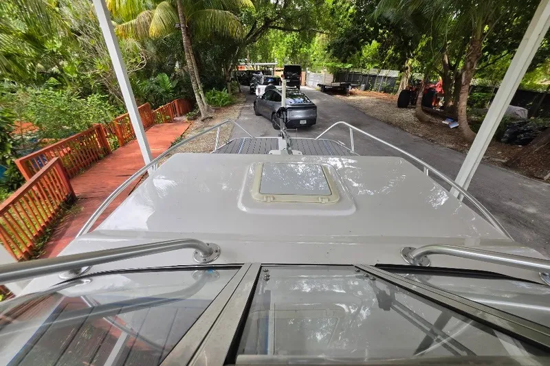 Slide: The Image of 2006 Twin Vee 26 Express boat docked, surrounded by lush greenery and parked vehicles. - 24