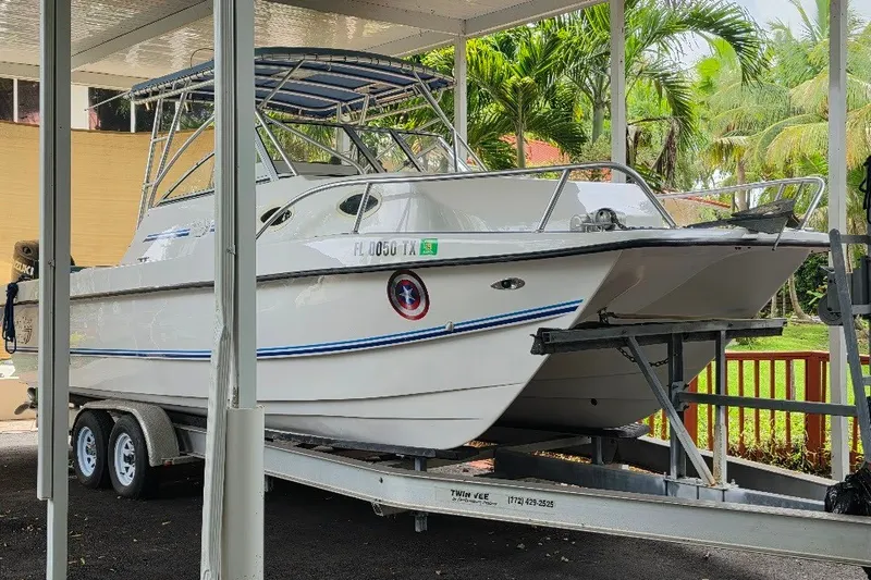 Slide: The Image of 2006 Twin Vee 26 Express boat on trailer, parked under a canopy with tropical background. - 4