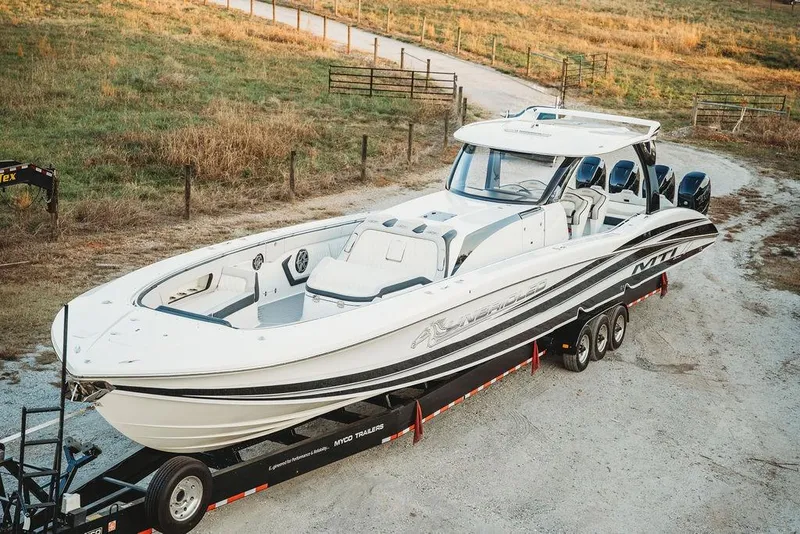 Slide: The Image of 2018 MTI 57 boat on trailer, parked on a gravel path near grassy field. - 2