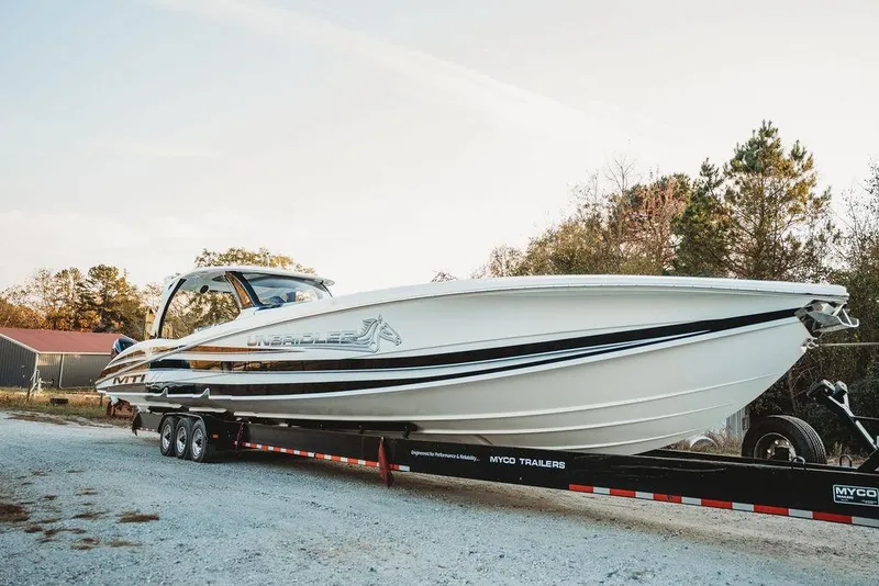 Slide: The Image of 2018 MTI 57 boat on trailer, parked outdoors with trees in background. - 14