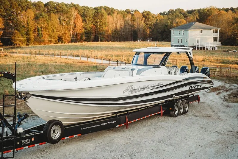 Slide: The Image of 2018 MTI 57 boat on trailer in rural setting, surrounded by autumn trees and a house. - 76