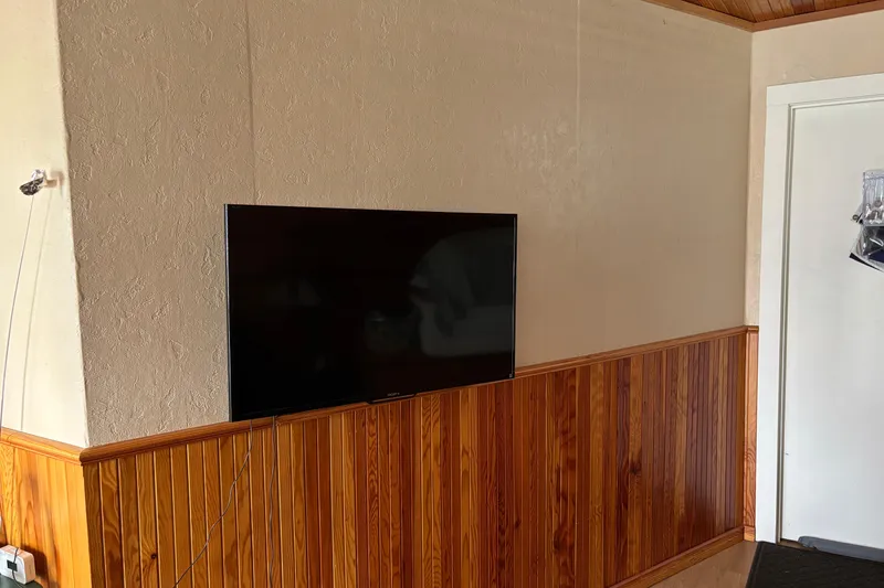 Slide: The Image of Wall-mounted TV on wood-paneled wall, next to a white door. - 15