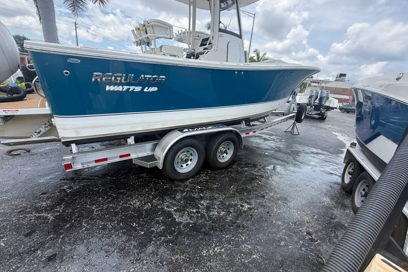 Slide: The Image of 2025 Regulator 25 boat on trailer, blue hull, parked outdoors. - 11