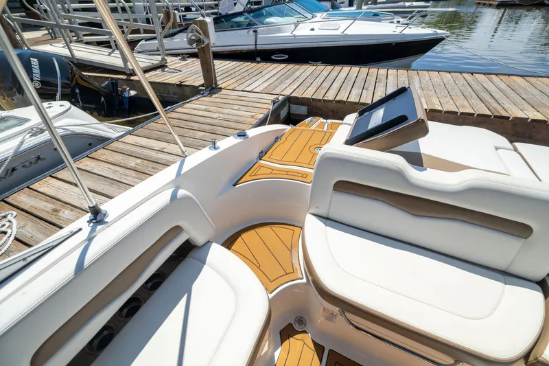 Slide: The Image of 2015 Chaparral 246 SSi boat interior with white seating and wooden deck at a marina. - 22