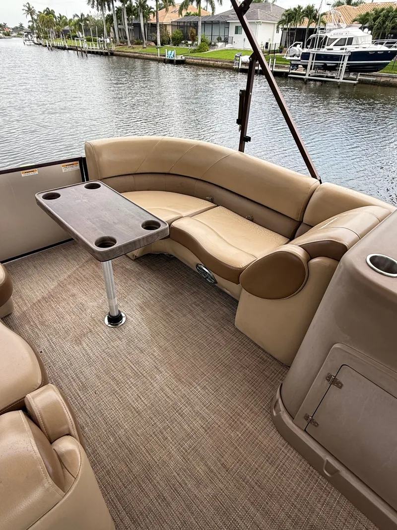 Slide: The Image of A sleek pontoon boat with beige upholstered seating and table, docked by the water. - 6