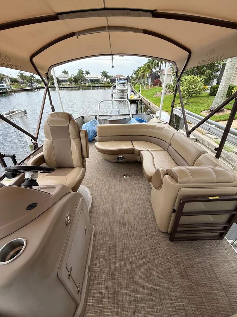 Slide: The Image of 2018 Veranda VVF25F2 pontoon boat with beige interior, curved seating, and bimini top, docked. - 12