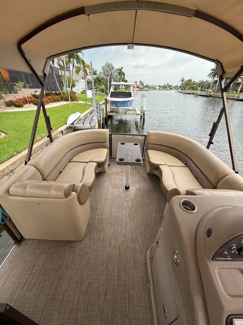 Slide: The Image of 2018 Veranda VVF25F2 pontoon boat with beige seating area and table, docked by the water. - 1