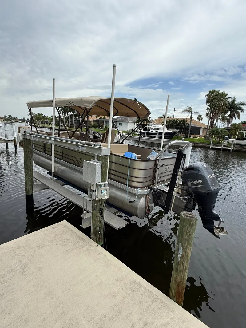 The Image of A 2018 Veranda VVF25F2 pontoon boat on a lift, surrounded by water and palm trees. - 0