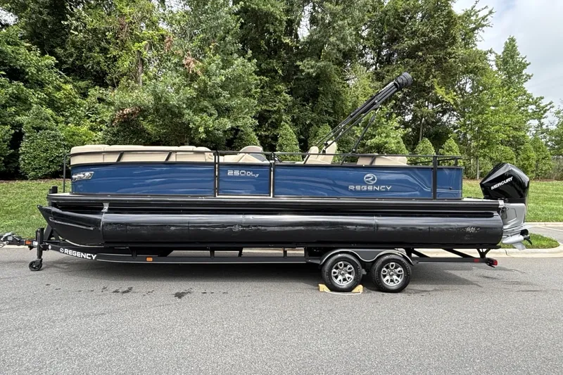 The Image of 2025 Regency 250DL3 pontoon boat on trailer, parked on a road with lush greenery. - 0