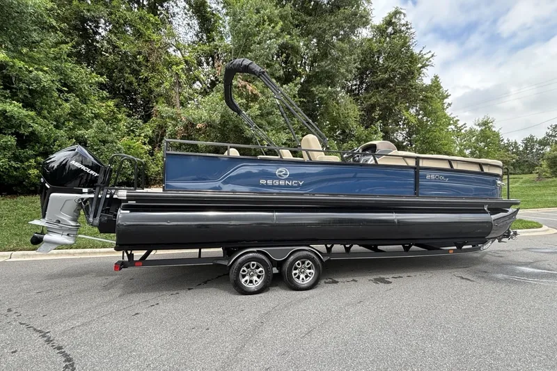 Slide: The Image of 2025 Regency 250DL3 pontoon boat on trailer, parked near lush greenery. - 13
