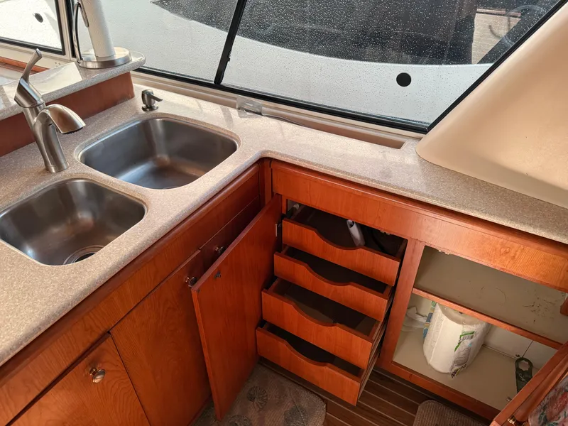 Slide: The Image of 2003 Meridian 490 Pilothouse kitchen with double sink, wooden cabinets, and open storage. - 14