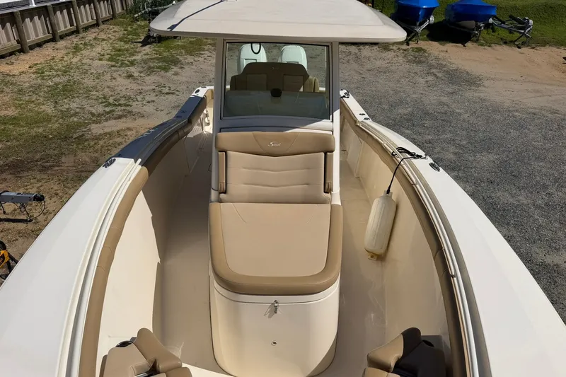 Slide: The Image of 2019 Scout 300 LXF boat with beige seating and white exterior, docked on gravel. - 6