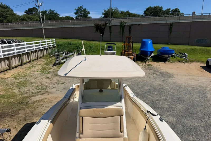 Slide: The Image of 2019 Scout 300 LXF boat parked on gravel near trailers and greenery. - 7