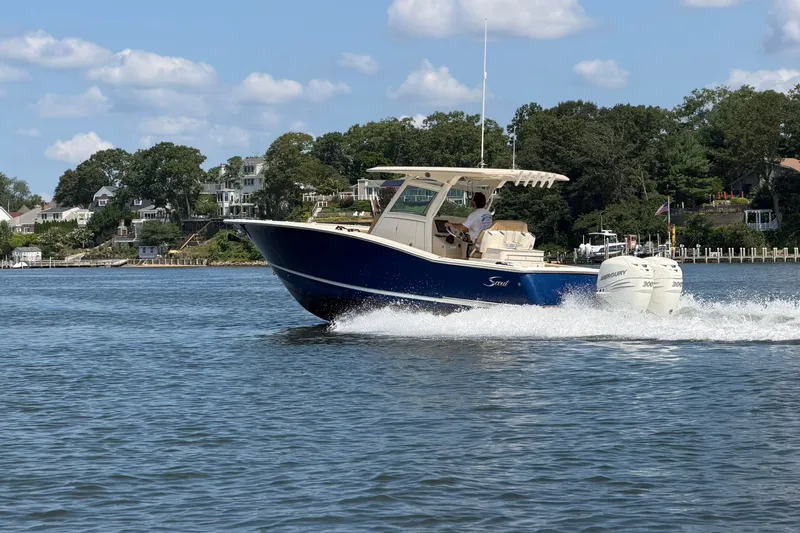 The Image of 2019 Scout 300 LXF boat cruising on a scenic lake with waterfront homes. - 0