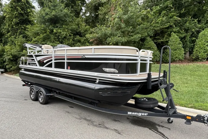 Slide: The Image of 2023 Ranger 223C pontoon boat on trailer, parked near lush greenery. - 13