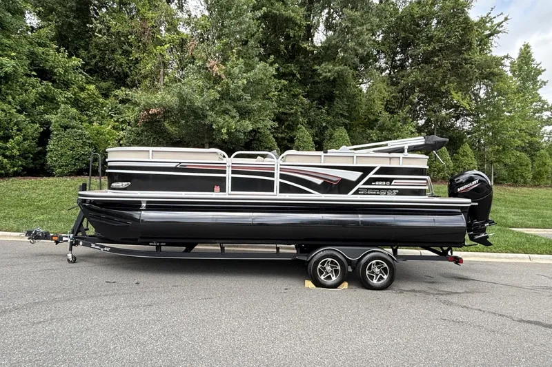 The Image of 2023 Ranger 223C pontoon boat on trailer, parked on road with lush green background. - 0