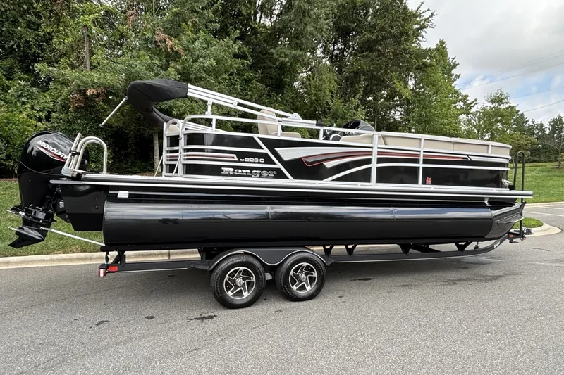 Slide: The Image of 2023 Ranger 223C pontoon boat on trailer, parked on a road with trees in background. - 14