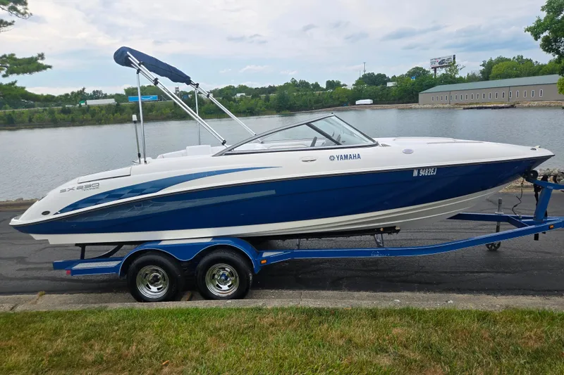 The Image of 2005 Yamaha Boats SX230 on trailer by a riverside, featuring sleek blue and white design. - 0