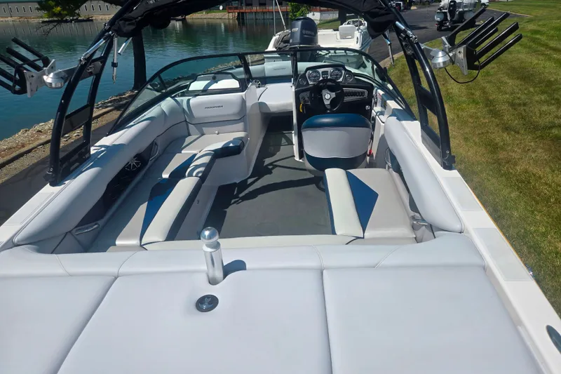 Slide: The Image of 2012 Moomba Mojo 2.5 boat interior with seating and steering wheel, docked by a lake. - 10