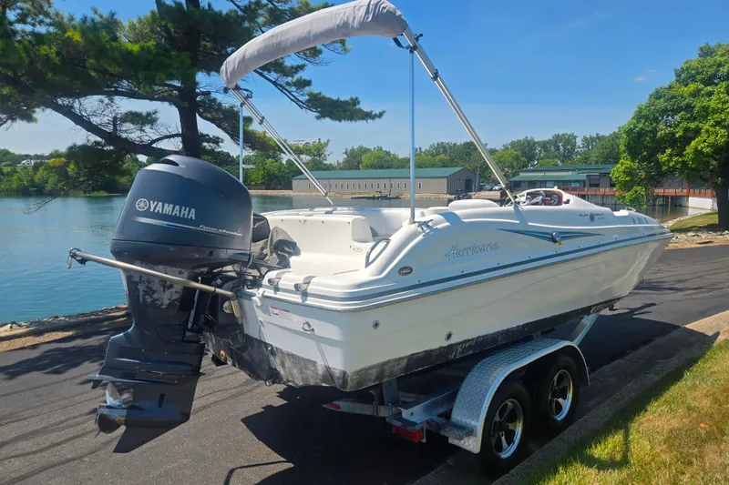 Slide: The Image of 2013 Hurricane SunDeck Sport 188 OB boat with Yamaha engine on trailer by a lake. - 1