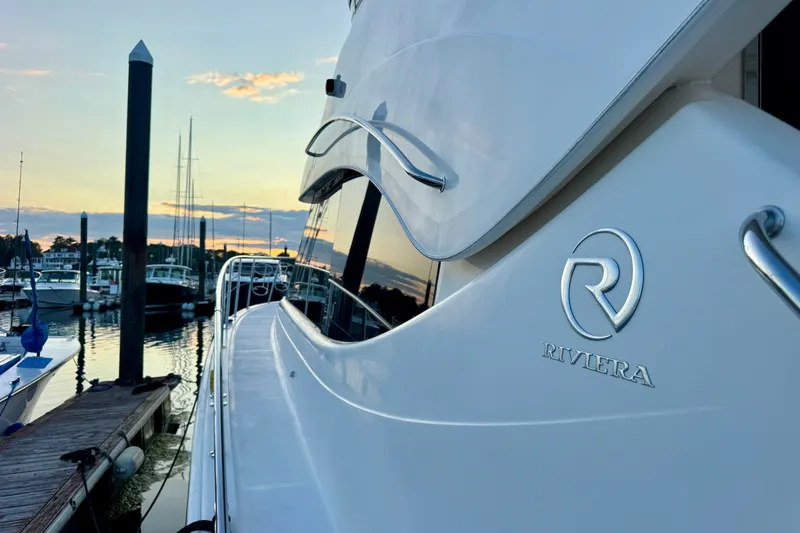 Slide: The Image of 2009 Riviera 45 Open Flybridge yacht docked at sunset, showcasing sleek design and logo. - 13