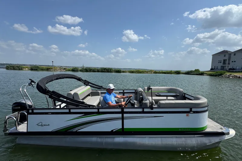 Slide: The Image of 2023 Qwest Lanai 820 pontoon boat on a sunny lake with a driver. - 2