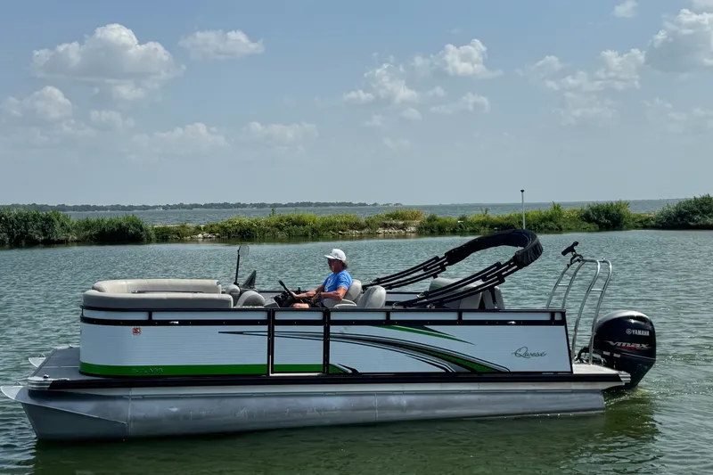 The Image of 2023 Qwest Lanai 820 pontoon boat on a serene lake under a partly cloudy sky. - 0