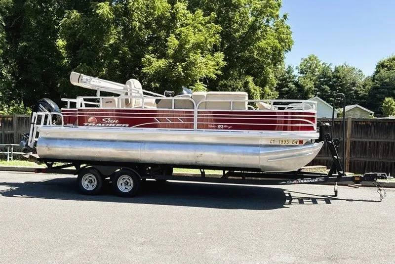 The Image of 2021 Sun Tracker Fishin' Barge 20 DLX pontoon boat on trailer, parked outdoors. - 0