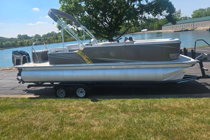 Slide: The Image of 2020 Avalon LSZ Cruise Rear Bench pontoon boat on trailer by a scenic river. - 9