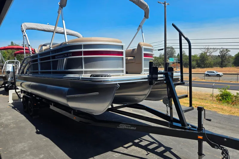 Slide: The Image of 2022 Bennington L24 pontoon boat on trailer, parked outdoors under clear blue sky. - 3