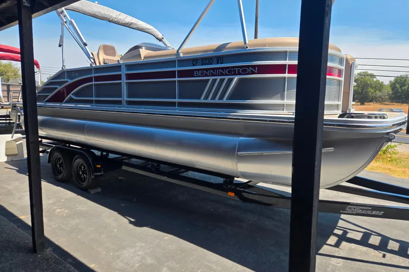 Slide: The Image of 2022 Bennington L24 pontoon boat on trailer, parked outdoors. - 2
