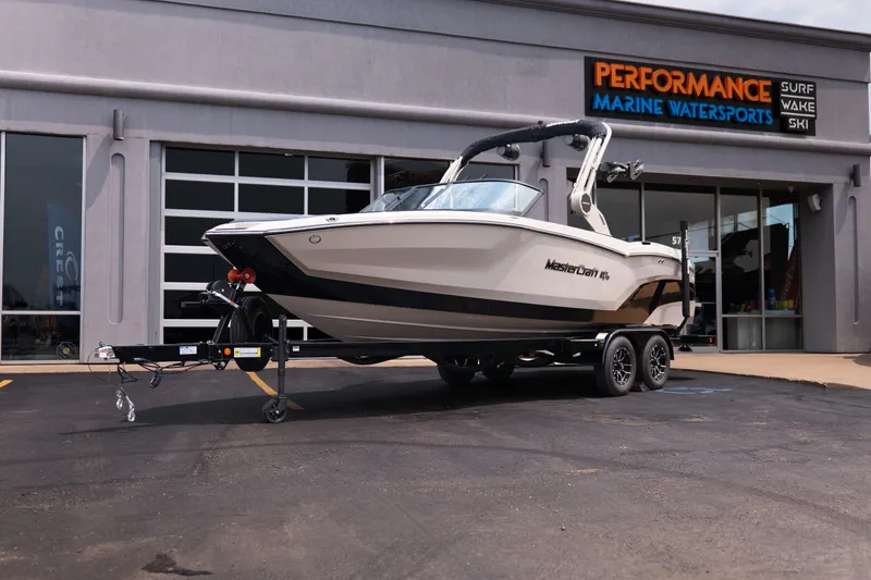 The Image of 2027 MasterCraft NXT23 boat on trailer outside Performance Marine Watersports store. - 1