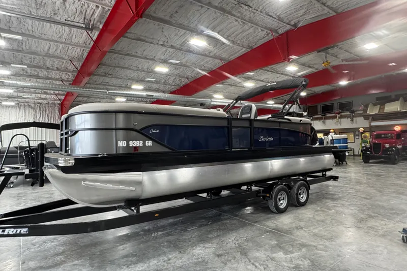 The Image of 2025 Barletta Cabrio 24QC pontoon boat on trailer in spacious indoor showroom. - 1