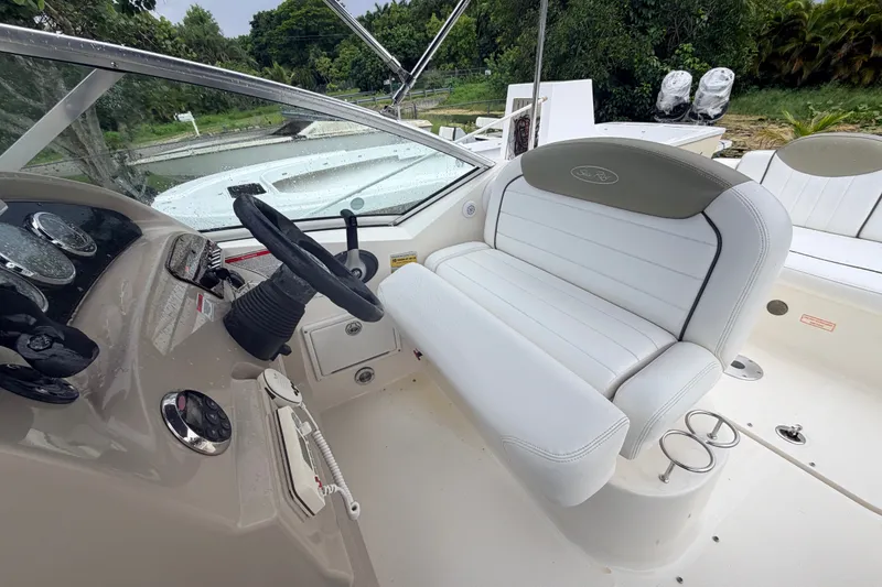 Slide: The Image of 2007 Sea Ray 240 Sundancer cockpit with white seating and steering wheel, surrounded by lush greenery. - 22