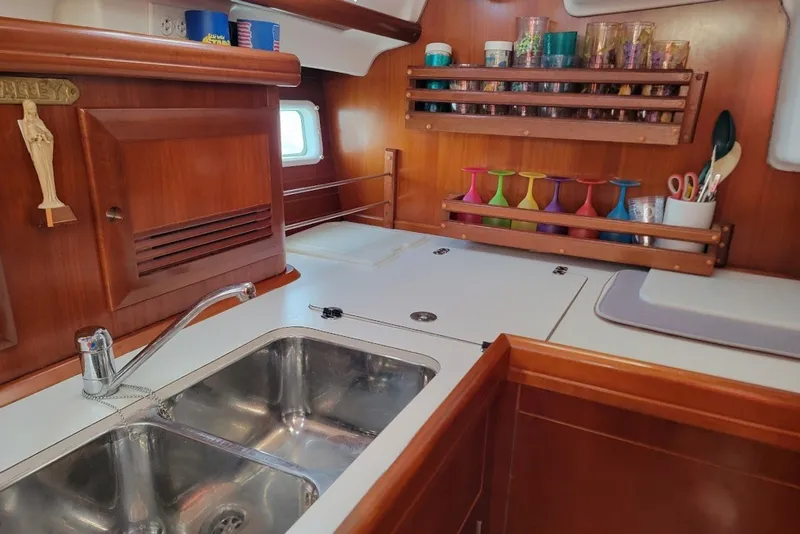 Slide: The Image of Galley kitchen in 2003 Beneteau 423 sailboat with wooden cabinetry and colorful glassware. - 29