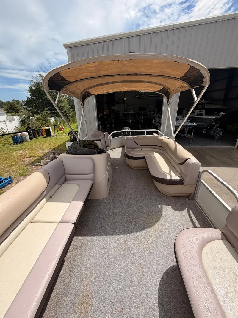Slide: The Image of A spacious pontoon boat with beige seating and a sun canopy, parked in a boatyard. - 14