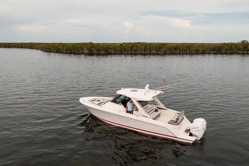 Slide: The Image of 2020 Tiara Sport 34 LS boat cruising on calm waters near a lush shoreline. - 2