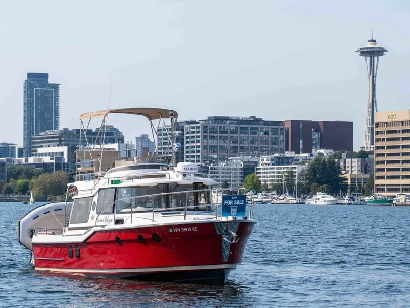 The Image of A red 2025 Ranger Tugs R-29 CB boat on the water with a cityscape in the background. - 1