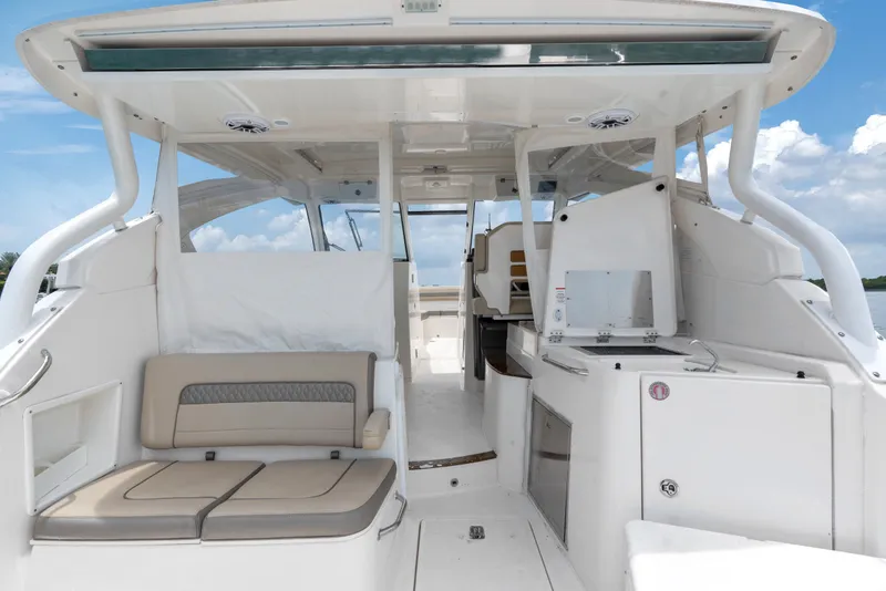 Slide: The Image of 2018 Pursuit DC 365 Dual Console boat interior with seating and kitchenette under a clear sky. - 30