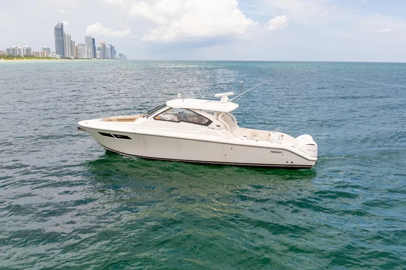Slide: The Image of 2018 Pursuit DC 365 Dual Console boat cruising on open water near city skyline. - 19
